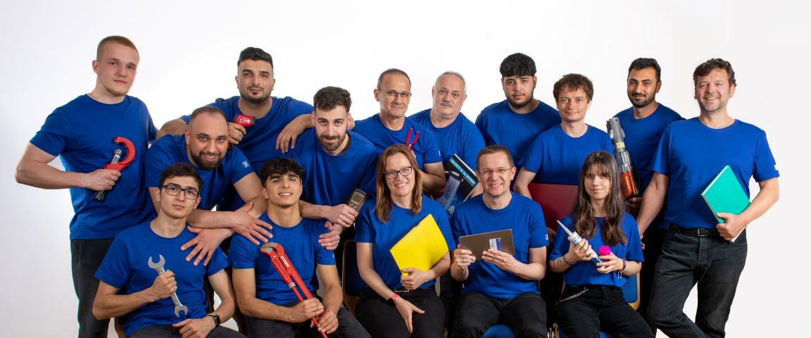 2023_Gruppenfoto Team der Gebrüder Weinlich in blauer Arbeitskleidung mit Werkzeugen und Planungsunterlagen